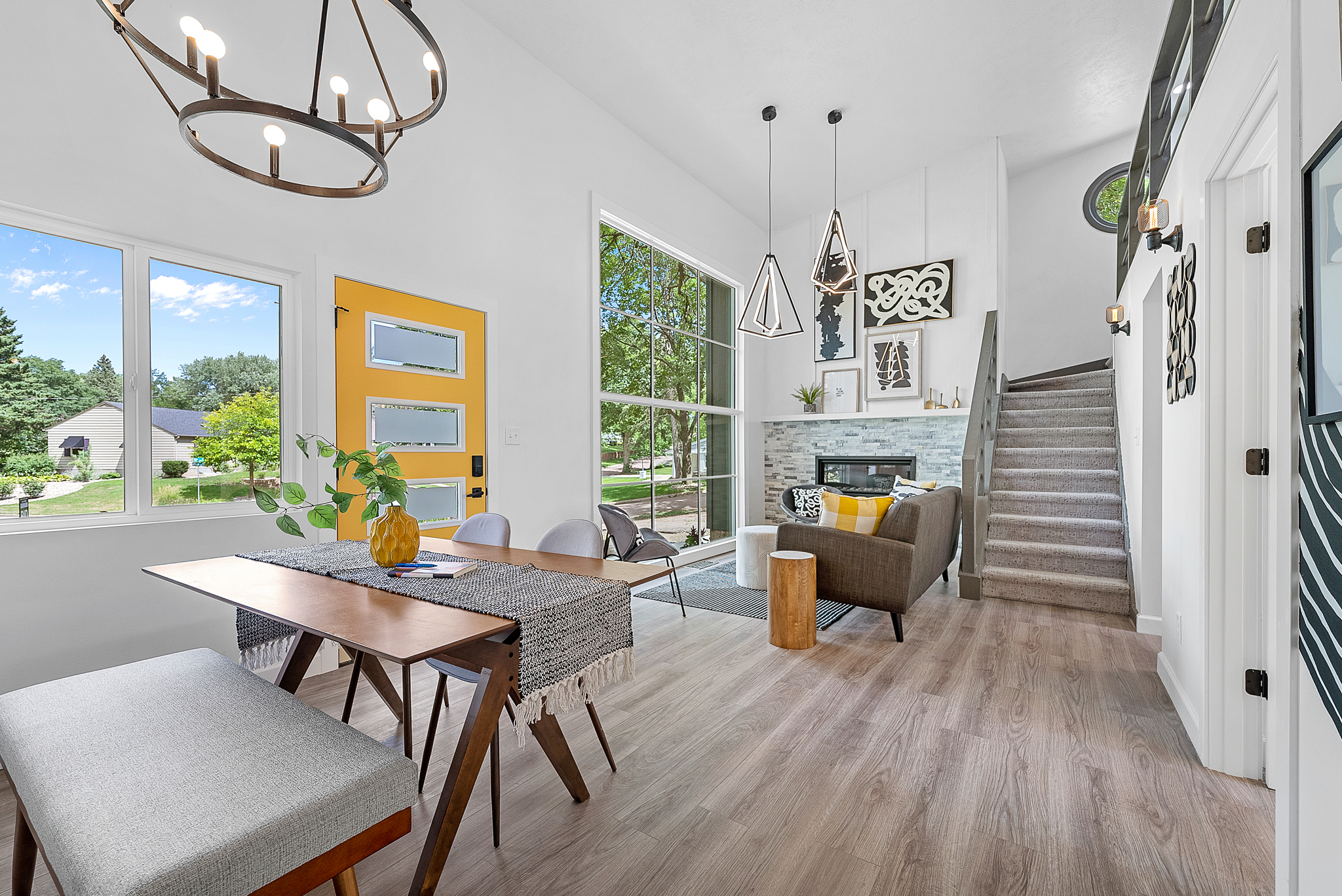 Contemporary home interior showing a staircase, fireplace, and a mix of wood and fabric furnishings, with a vibrant yellow door.