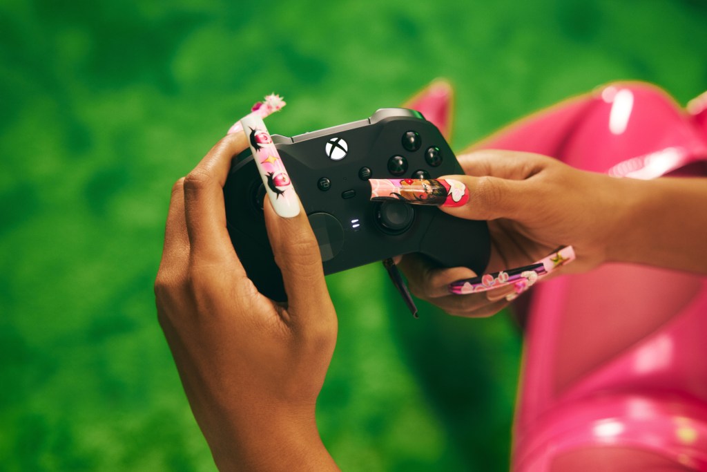 Close-up of hands with long, decorated nails holding a gaming controller against a green background.