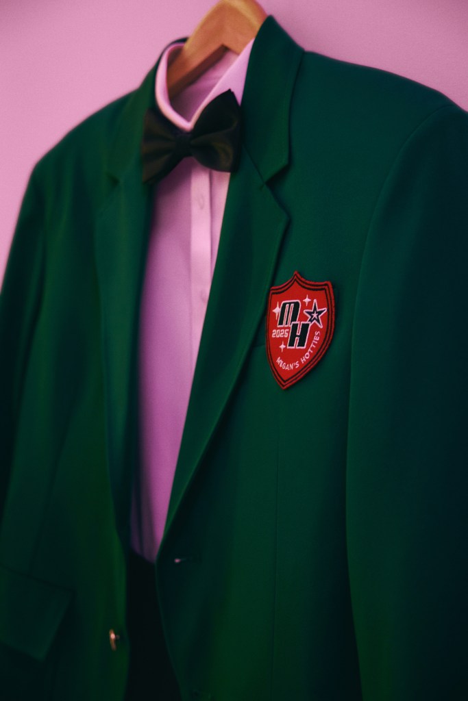 Green blazer with a red patch that reads '2025 MH Megan's Hotties' on a hanger.