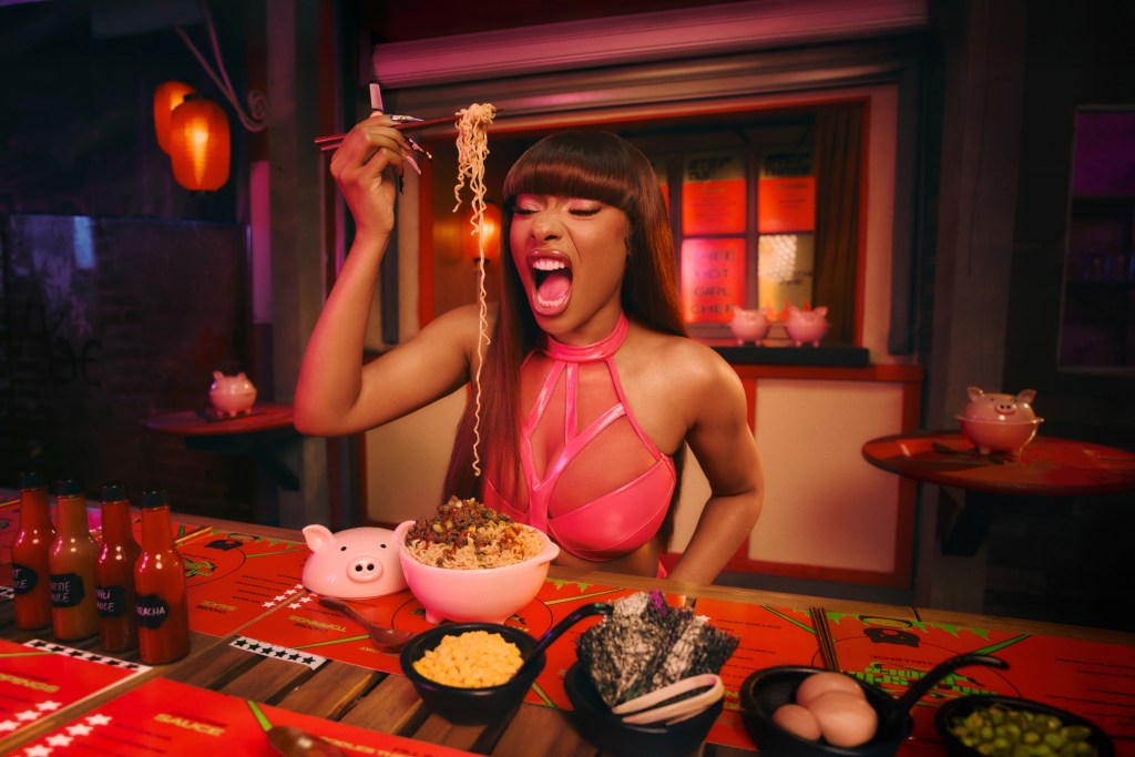 Woman in a pink halter top holding chopsticks with noodles over a bowl of ramen.