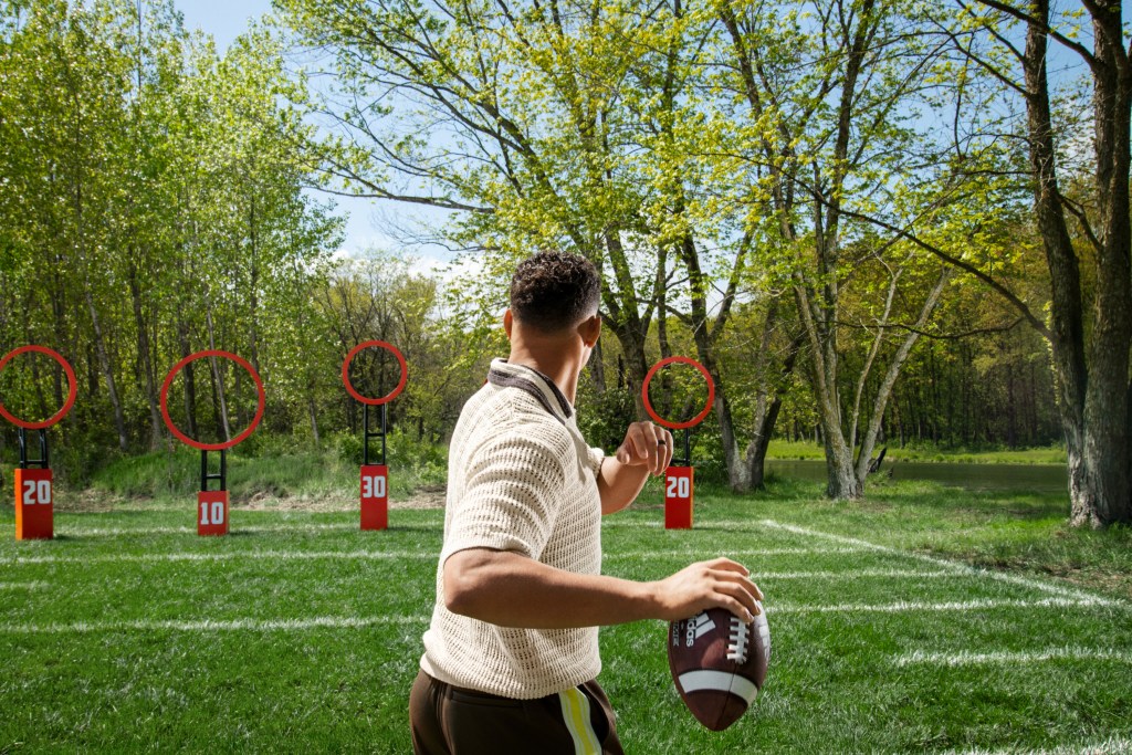 Person holding a football, aiming at circular targets on a grassy field surrounded by trees.