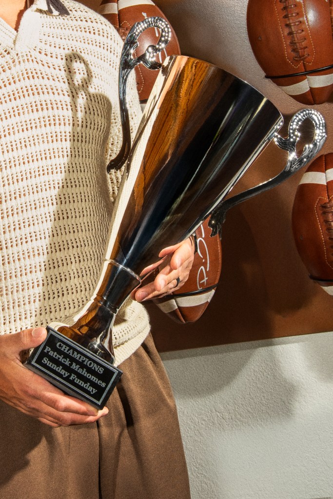 Close-up of a person holding a trophy labeled 'Champions Patrick Mahomes Sunday Funday,' with footballs in the background.