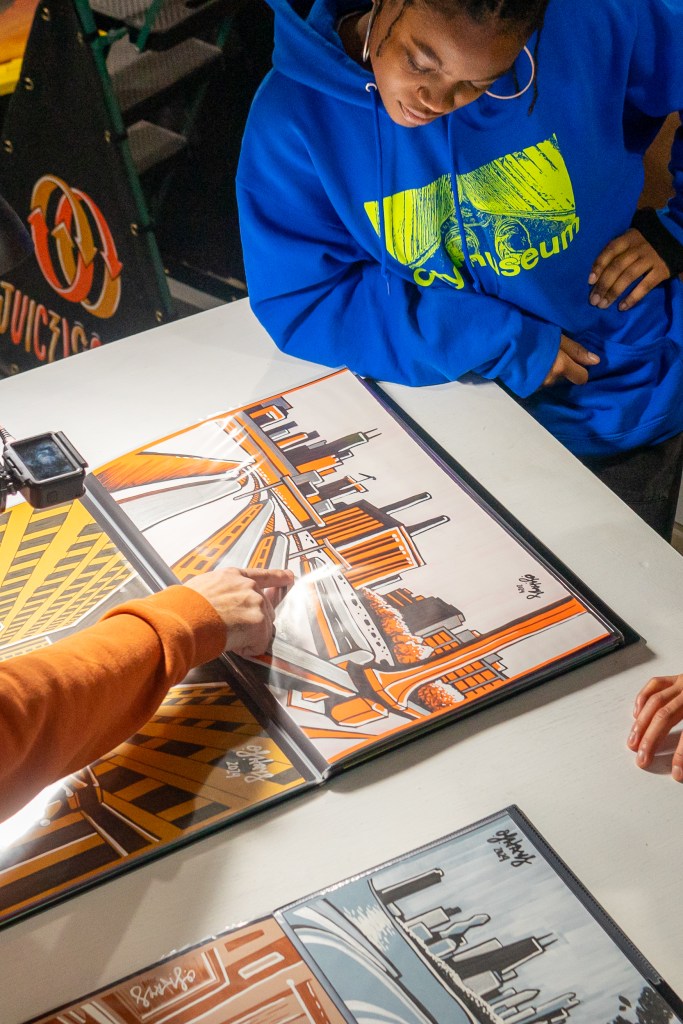 Person in blue hoodie observes colorful cityscape artwork on a table.