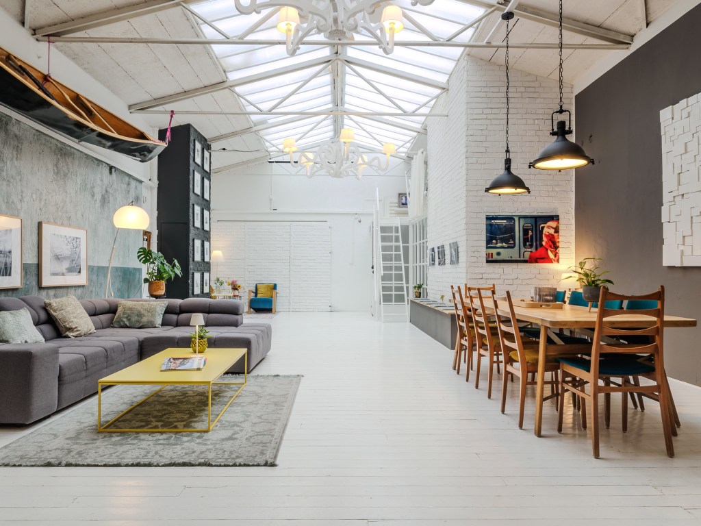 Spacious loft featuring a large sectional sofa, dining table, and modern decor under a skylit ceiling.