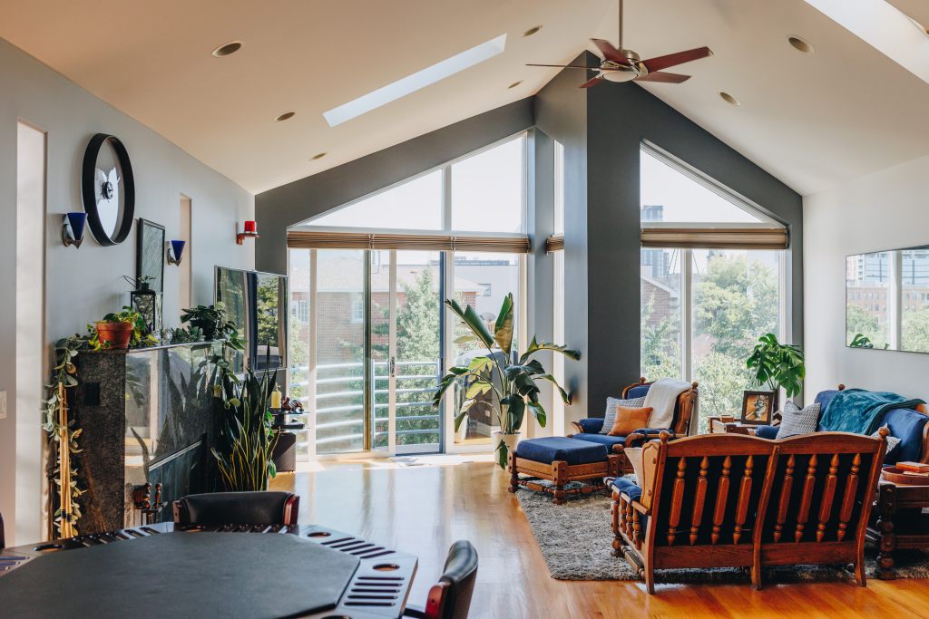 Spacious living room with large windows, wooden furniture, and indoor plants.