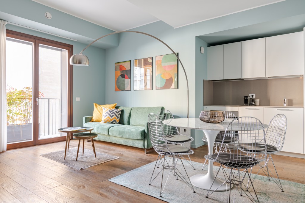 Bright modern living space with a mint green sofa, abstract artwork, and a small dining area.