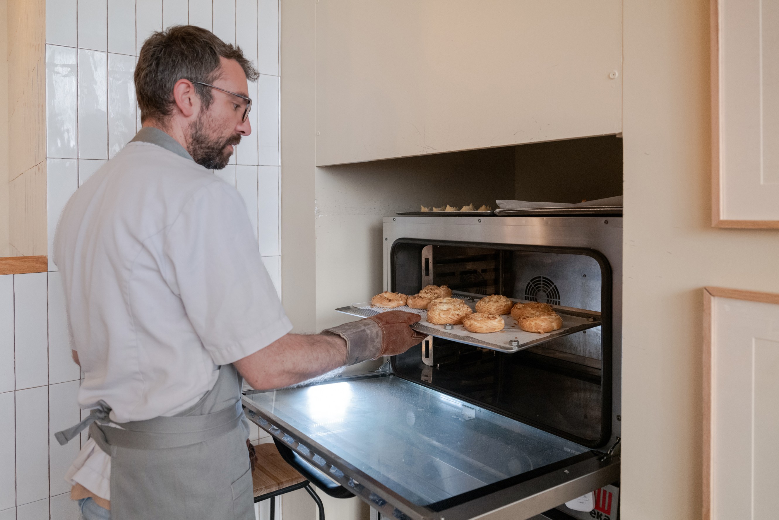 A person is placing a tray of freshly baked pastries into an oven.
