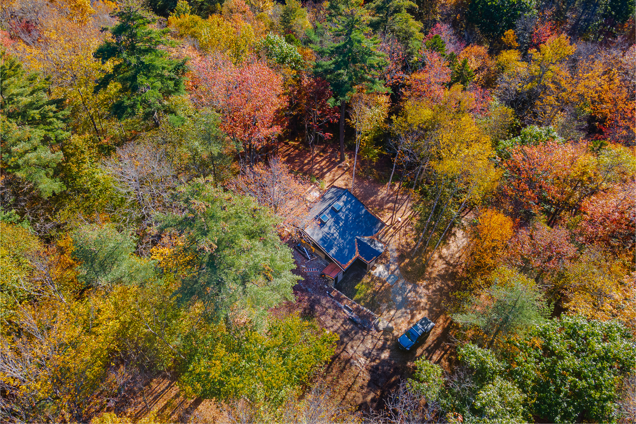 An aerial view shows a secluded cabin nestled among vibrant autumn foliage in a dense forest.