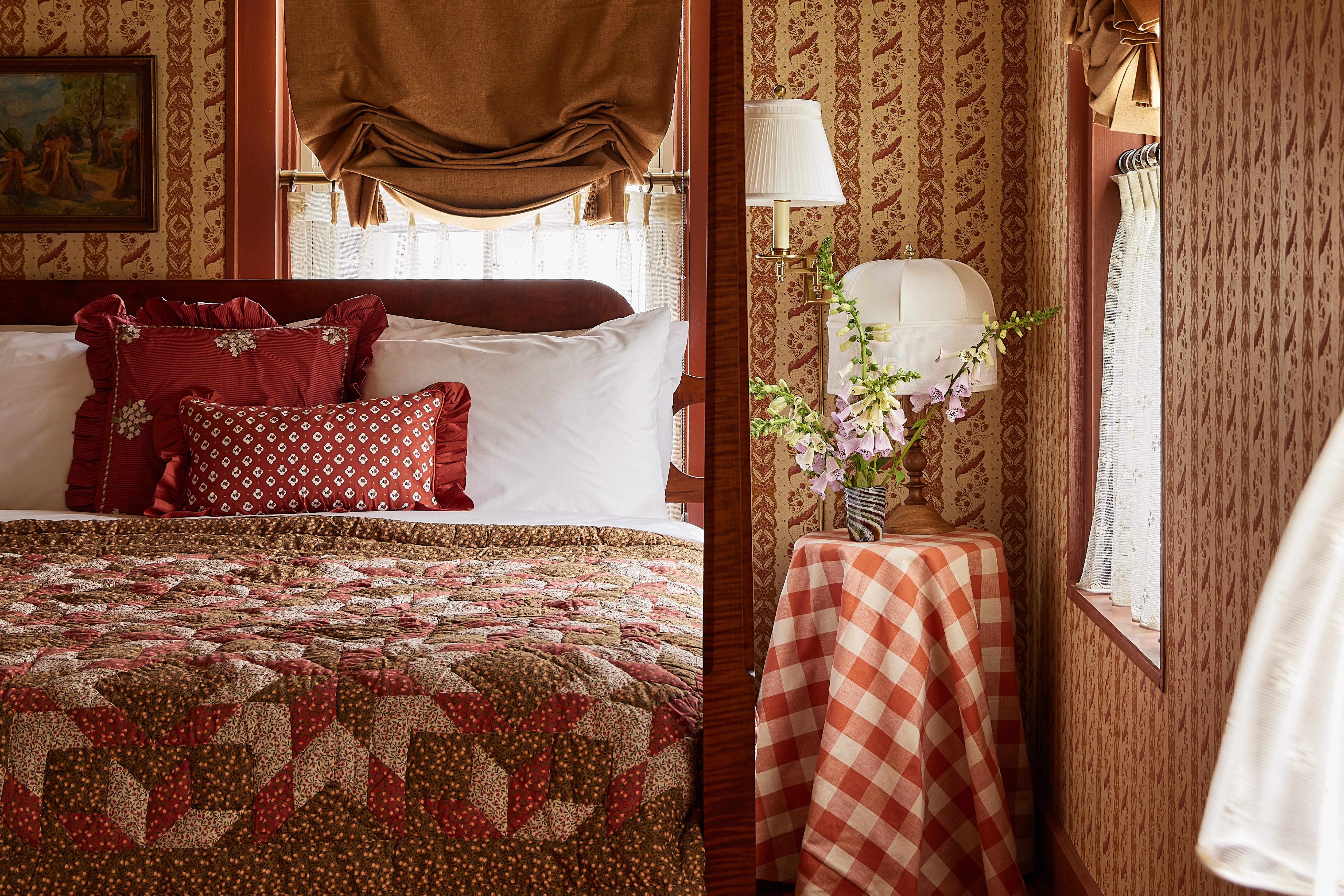 A cozy bedroom features patterned wallpaper, a patchwork quilt, and a rustic, vintage-inspired decor.