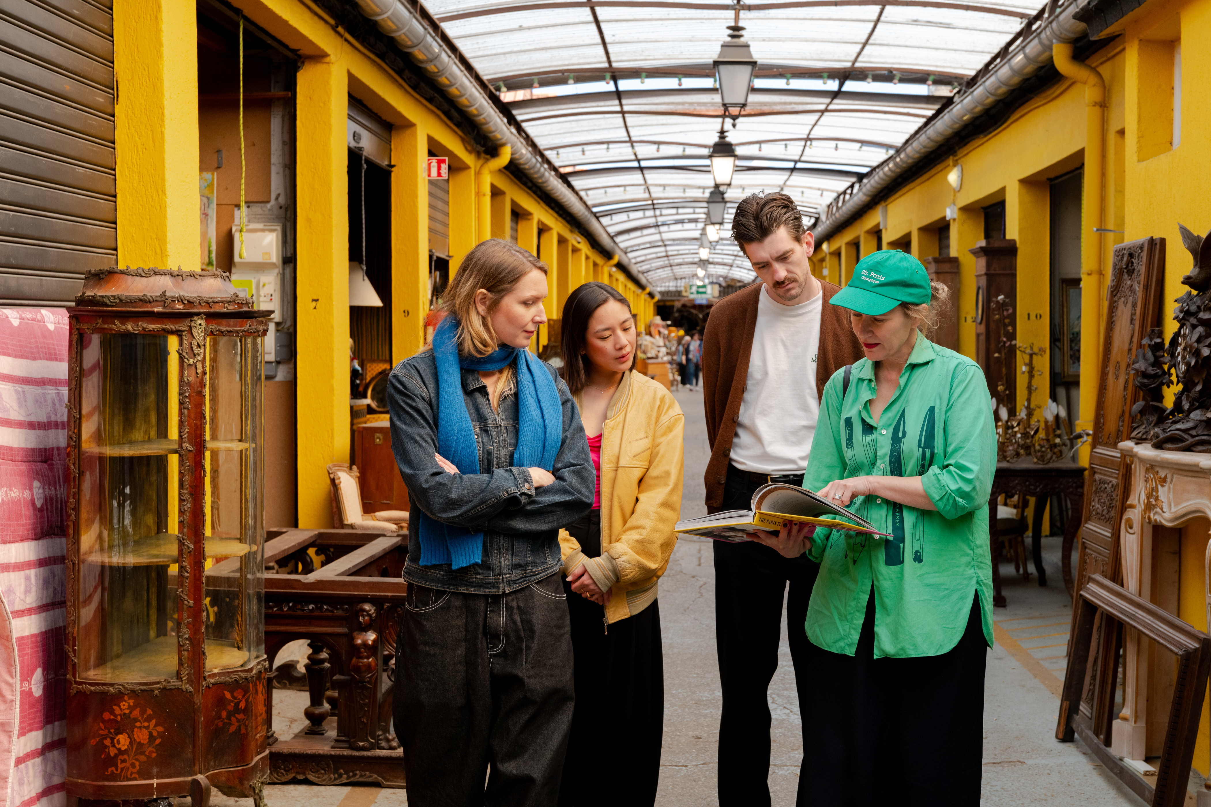 A group of people are gathered in a vibrant market, looking at a book together.