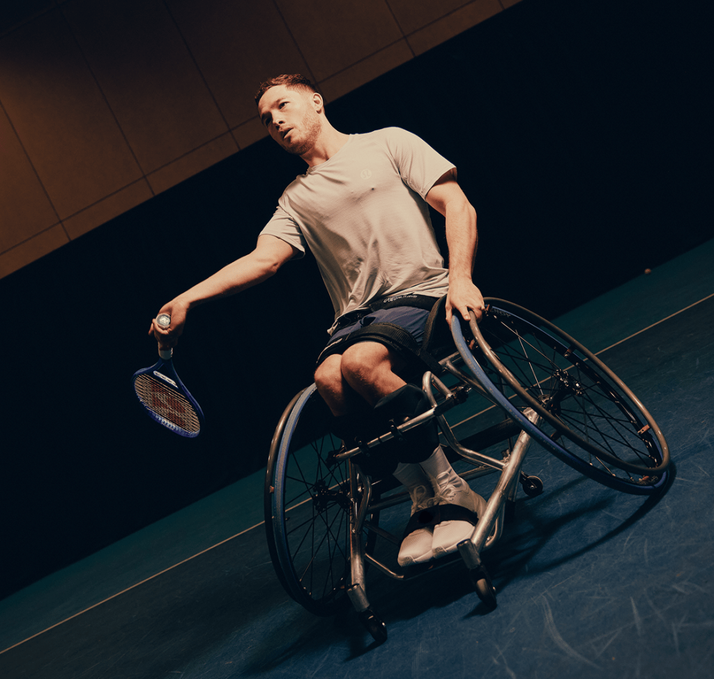 An athlete in a wheelchair prepares to serve a tennis ball during an indoor match.
