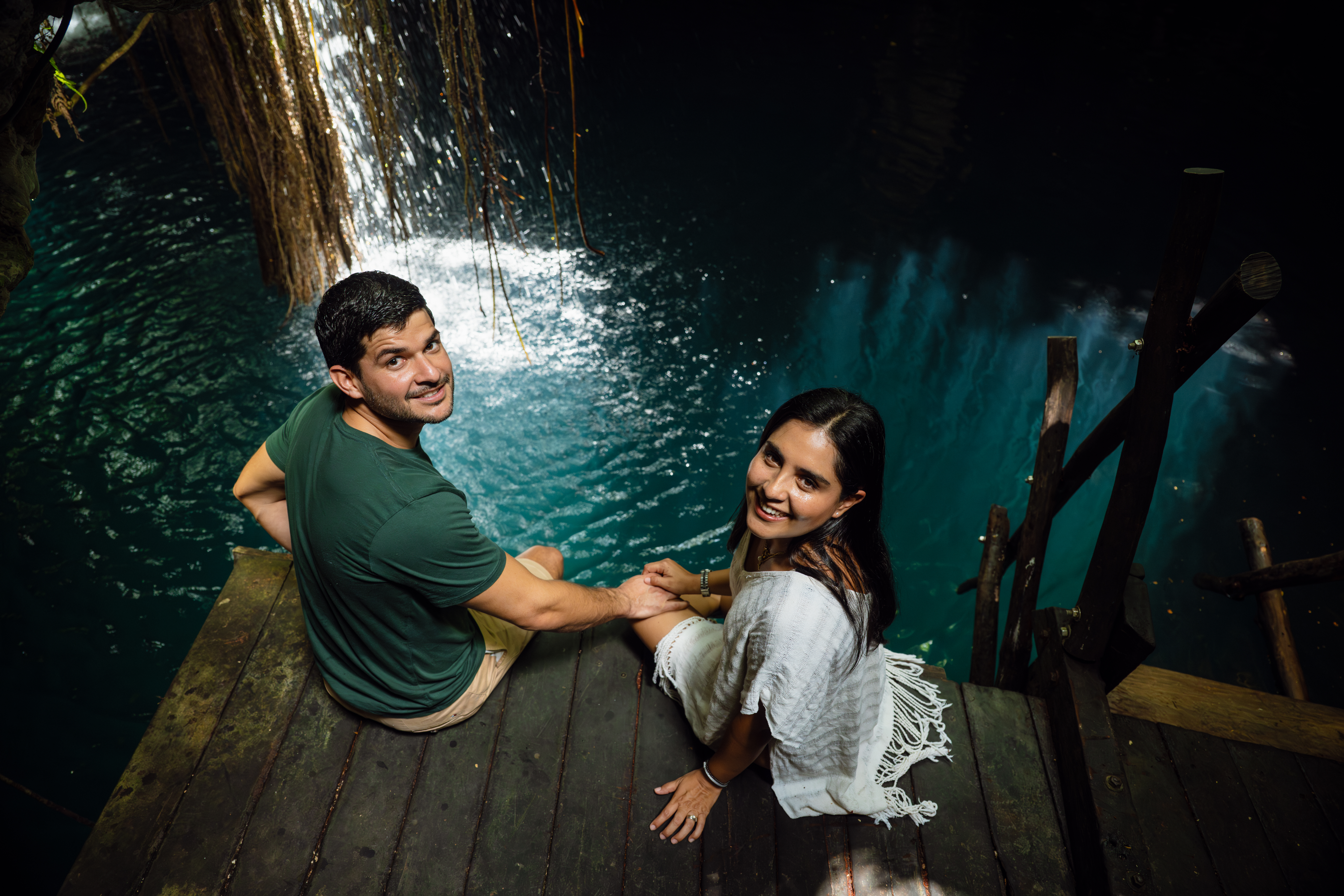 Pareja de hombre y mujer sosteniendo manos sentados al borde de un cenote