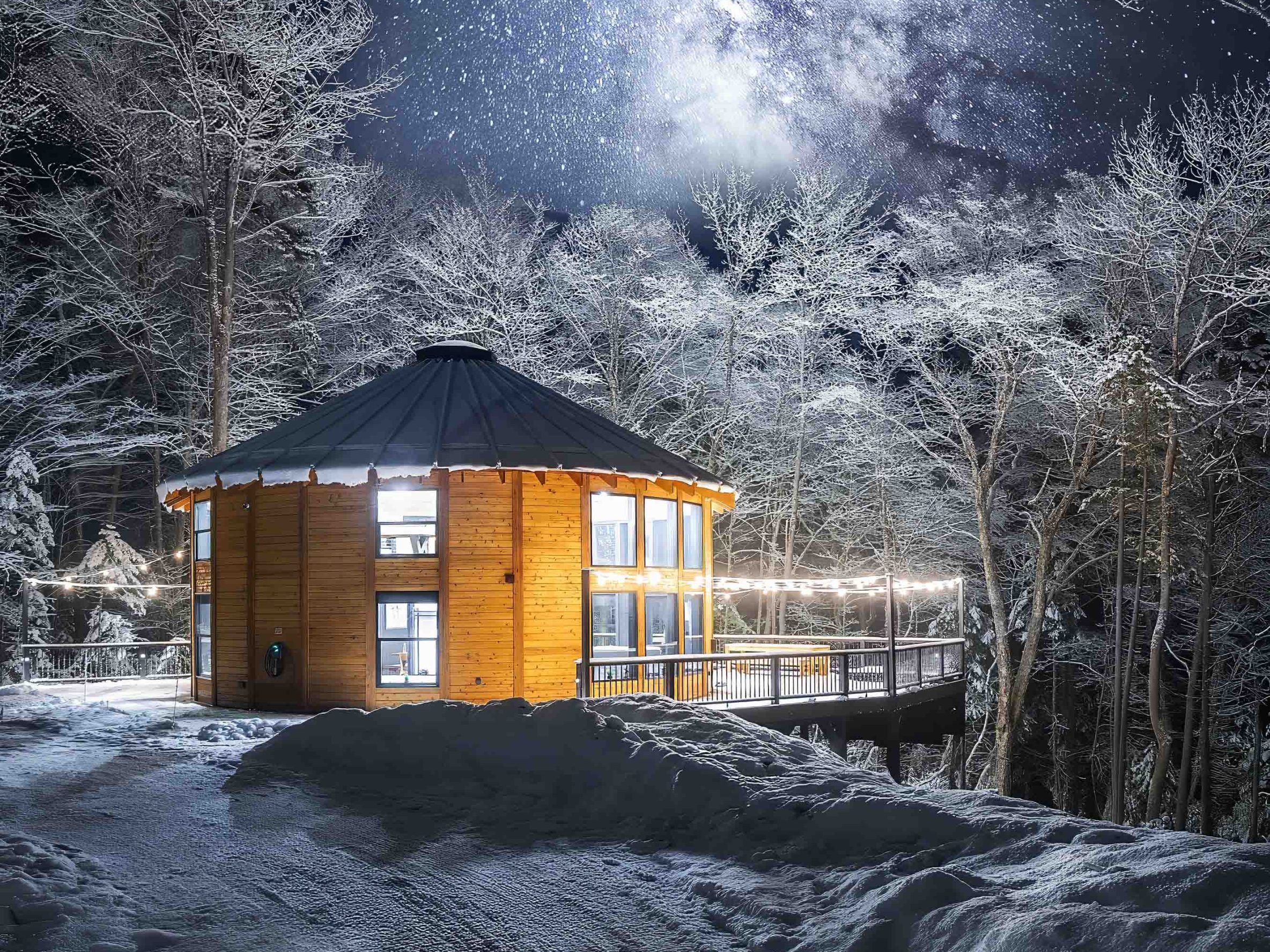 A mountain yurt surrounded by snow with Northern Lights above it.
