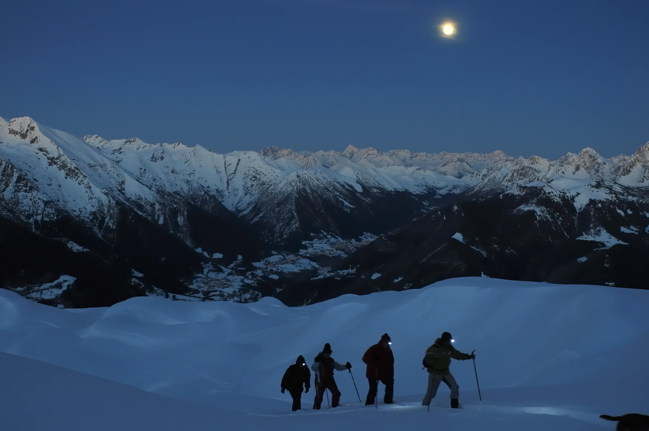 A group snowshoeing in the dark on a mountain.