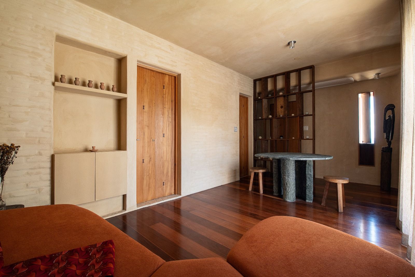 An earthy-toned living space features a cozy sofa, polished wooden floors, and minimalist decor with natural textures and artisanal pottery.