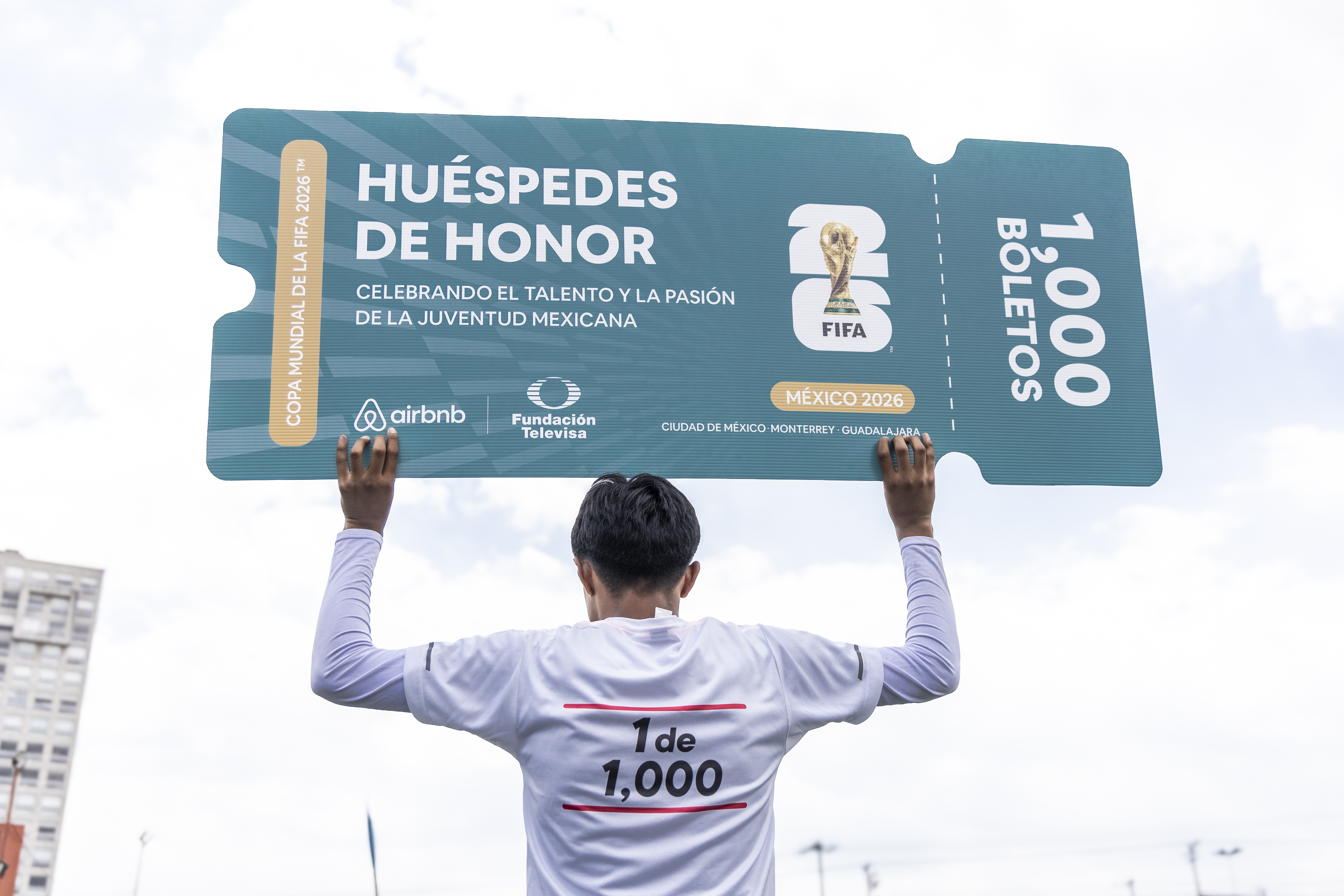 Hombre de espaldas sostiene un boleto gigante de Huespedes de Honor de la Copa Mundial de la FIFA 2026