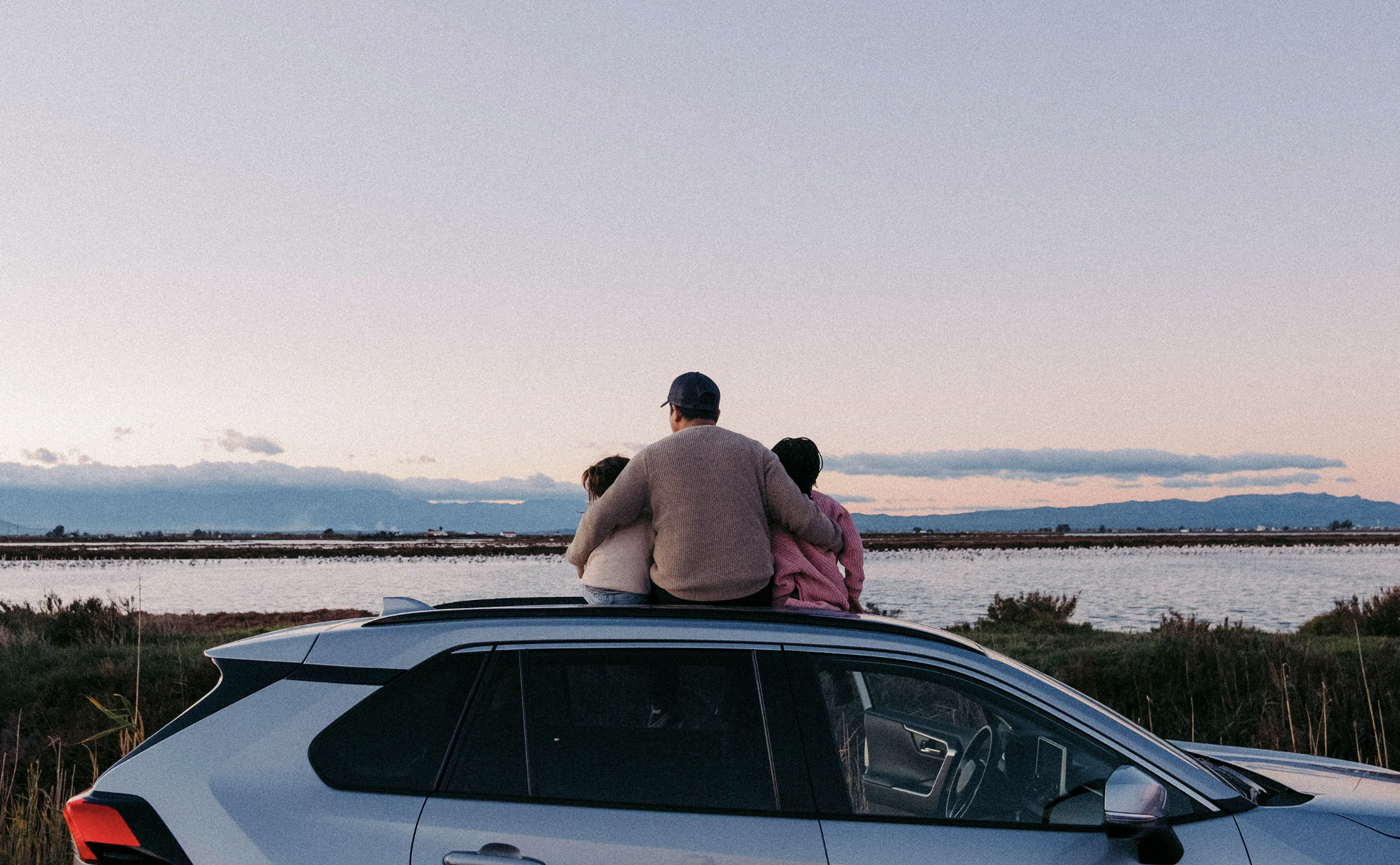 Foto de una familia sentada en la parte de encima de una camioneta mirando hacia el mar